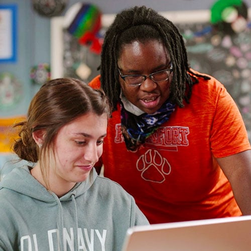Two people look at a laptop.