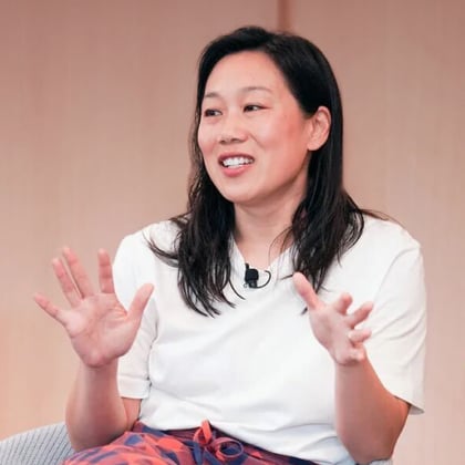 Priscilla Chan sits in a chair and gestures with her hands. She wears a black and red checkered skirt and a white T-shirt.