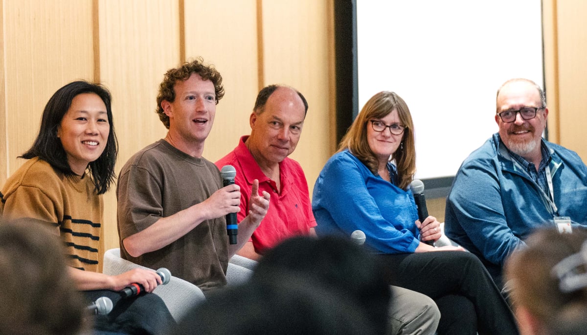 A panel of five people seated and holding microphones, engaged in a discussion; Mark Zuckerberg is speaking while the others listen attentively and smile.